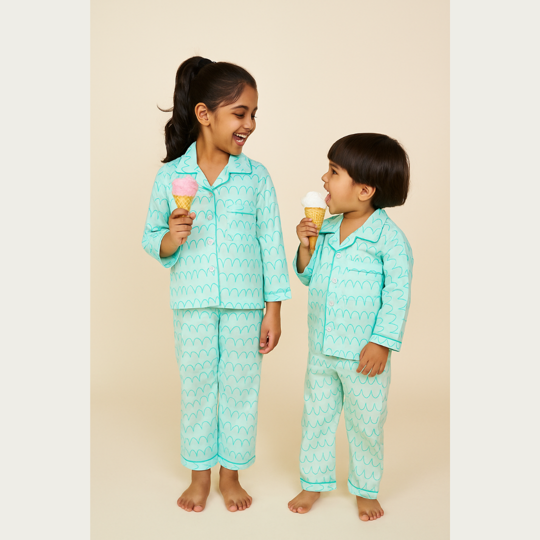 Two children in matching teal pajama sets holding ice cream cones on a beige background