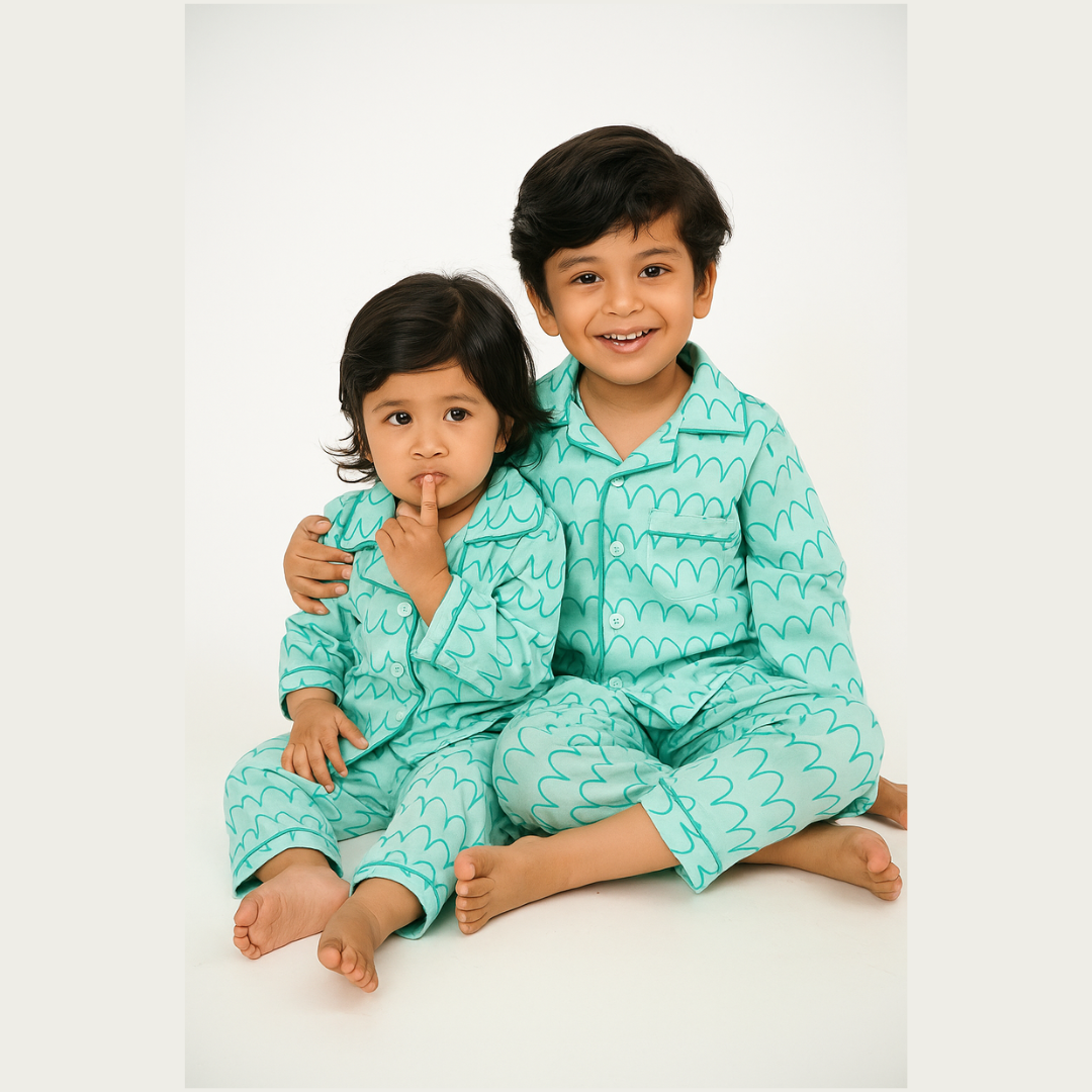 Two children wearing matching teal pajamas with a heart pattern on a white background